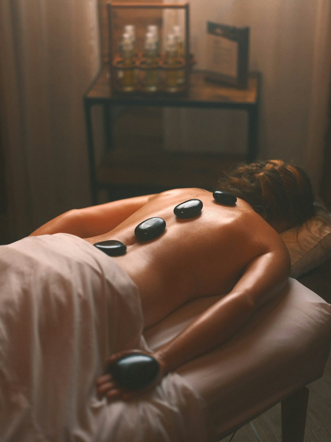 services-04 a-woman-laying-on-a-bed-with-hot-stones-on-her-back-tyra1ruaii